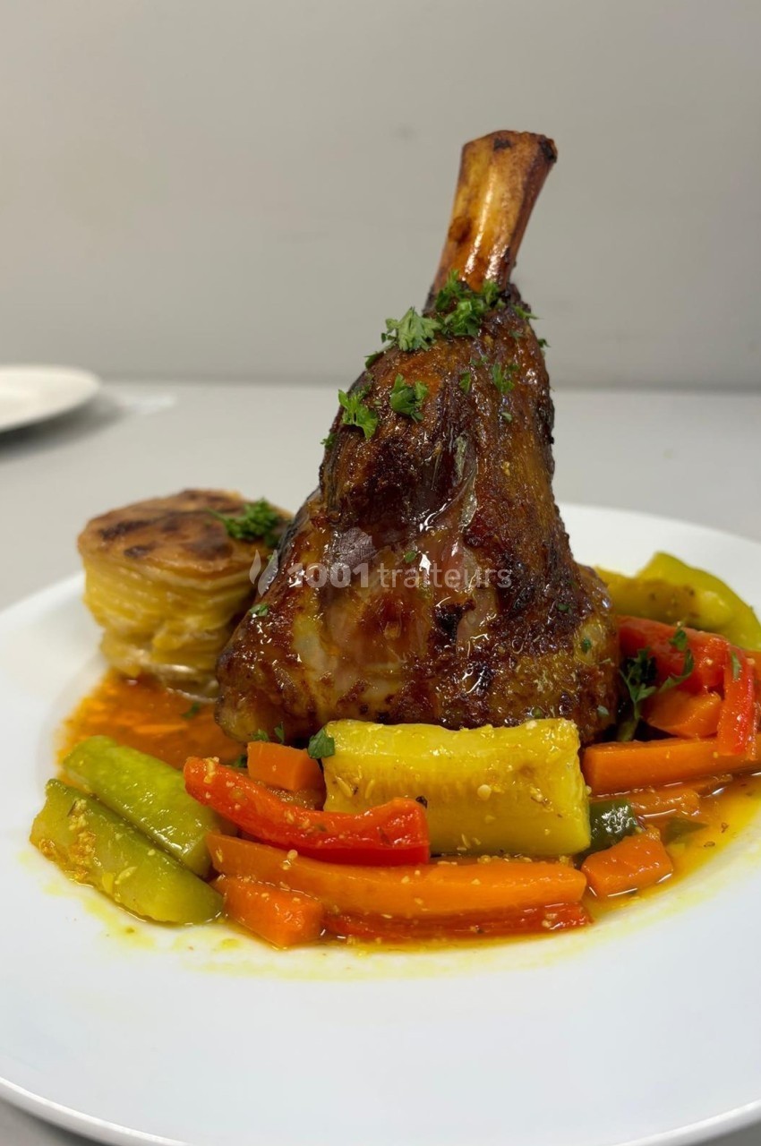 Jarret d'agneau braisé servi avec légumes colorés et gratin dauphinois sur une assiette blanche.