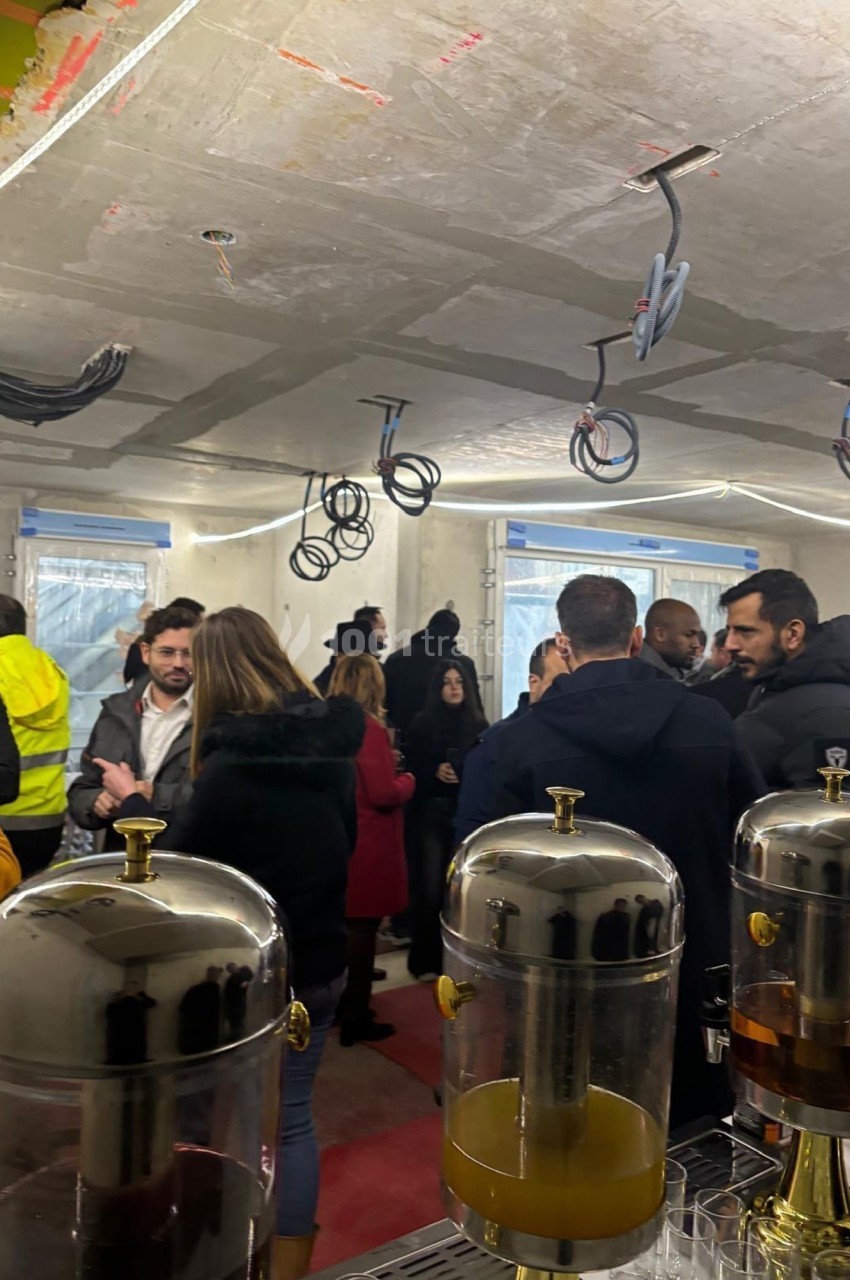 Groupe de personnes discutant dans un espace en construction, avec des distributeurs de boissons au premier plan.