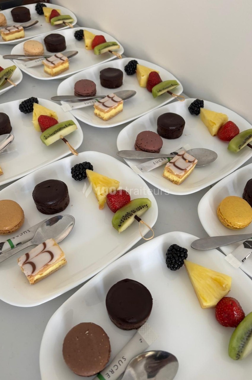 Assortiment de desserts sur des assiettes blanches, comprenant fruits frais, macarons et pâtisseries individuelles.