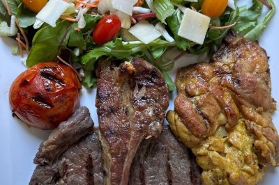 Assiette de burrata garnie de tomates cerises colorées et décorée d'une fleur violette sur une table blanche.