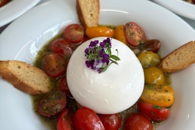 Assiette de burrata garnie de tomates cerises colorées et décorée d'une fleur violette sur une table blanche.