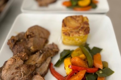 Assiette de burrata garnie de tomates cerises colorées et décorée d'une fleur violette sur une table blanche.