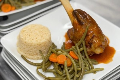 Assiette de burrata garnie de tomates cerises colorées et décorée d'une fleur violette sur une table blanche.