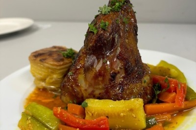 Assiette de burrata garnie de tomates cerises colorées et décorée d'une fleur violette sur une table blanche.