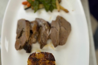 Assiette de burrata garnie de tomates cerises colorées et décorée d'une fleur violette sur une table blanche.
