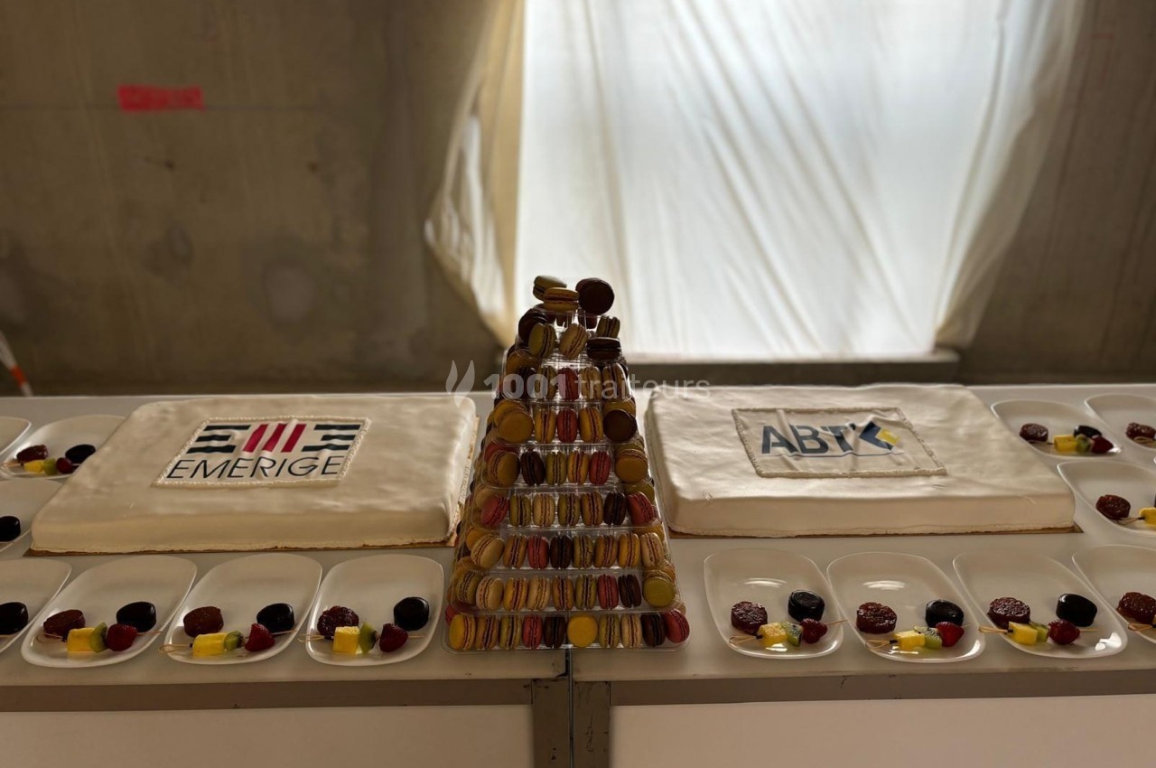 Deux gâteaux décorés avec des logos et une pyramide de macarons, entourés d'assiettes de desserts variés.