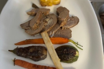 Assiette de burrata garnie de tomates cerises colorées et décorée d'une fleur violette sur une table blanche.