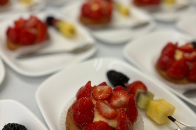 Assiette de burrata garnie de tomates cerises colorées et décorée d'une fleur violette sur une table blanche.
