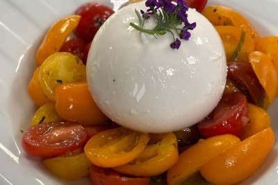 Assiette de burrata garnie de tomates cerises colorées et décorée d'une fleur violette sur une table blanche.