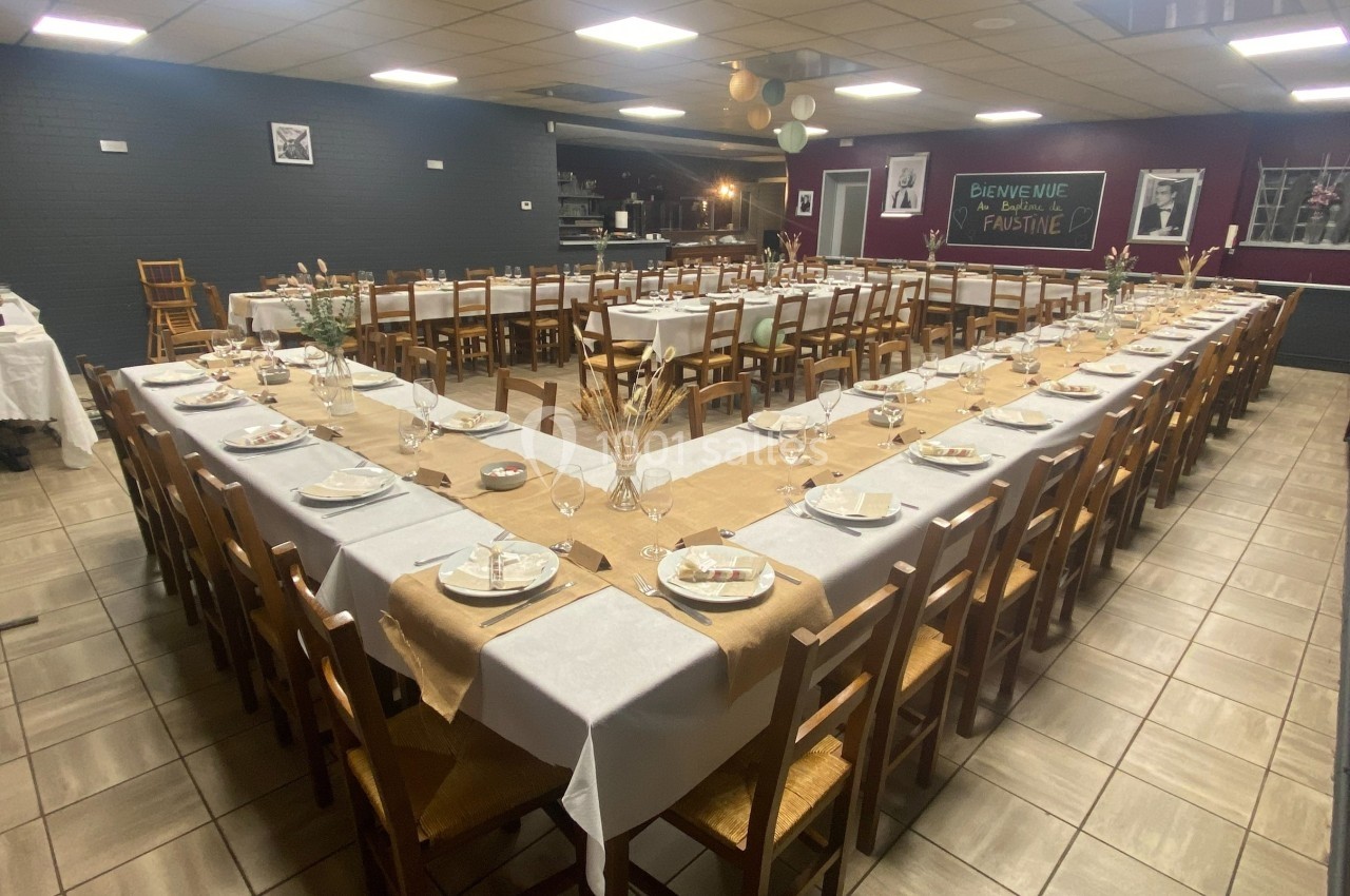 Salle de réception avec tables en U dressées de nappes blanches, décorations simples et assiettes disposées.