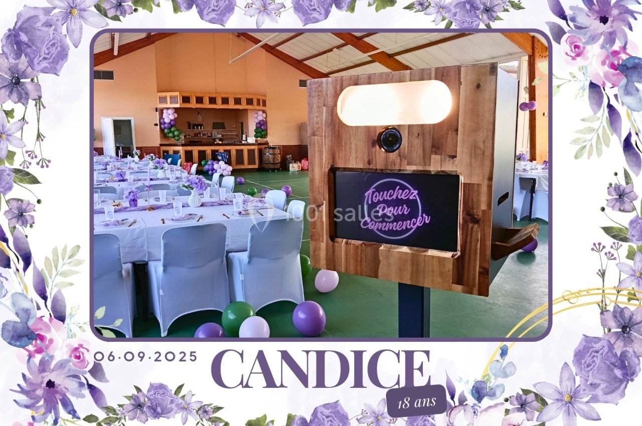 Photobooth en bois dans une salle décorée pour une fête, avec des tables dressées et des ballons colorés.