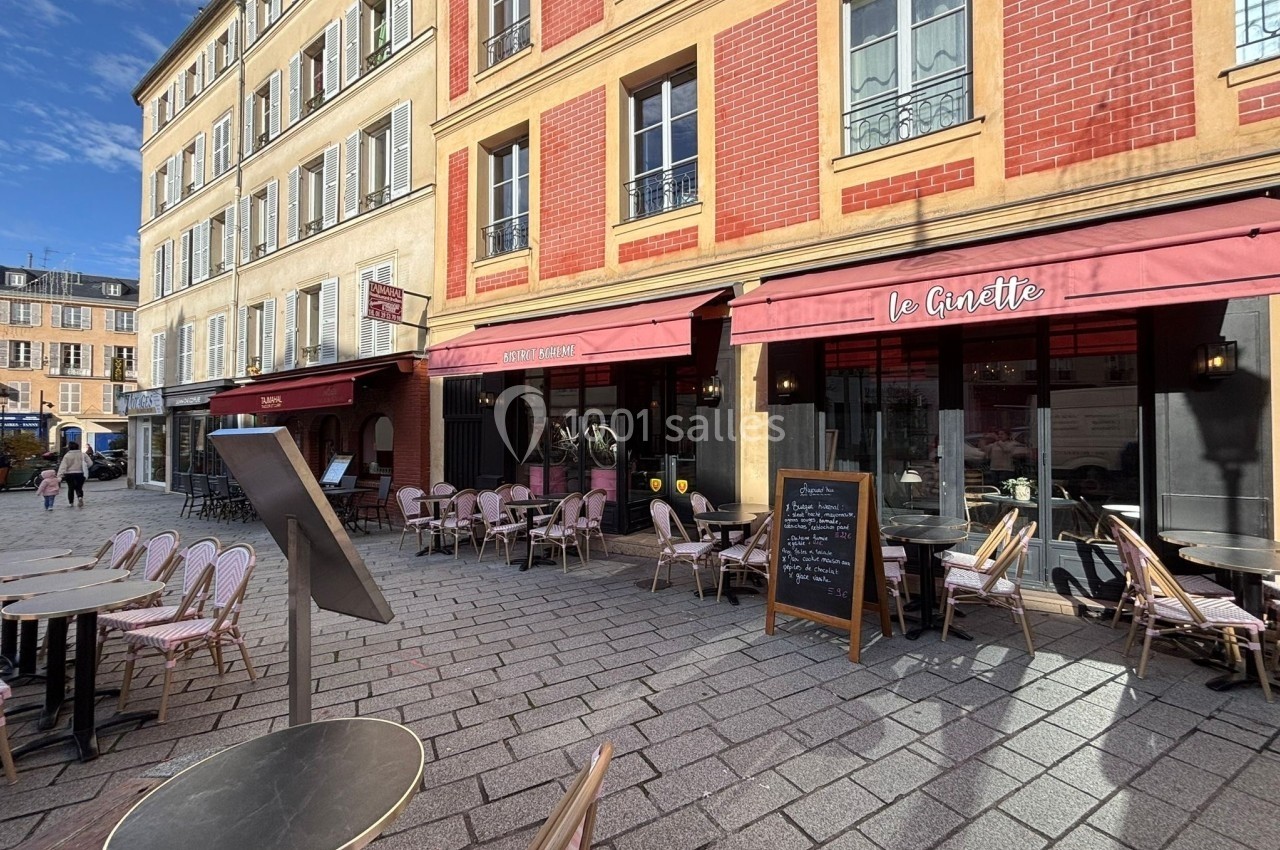 Terrasse de café avec tables et chaises en plein air devant une façade en briques rouges sous un ciel dégagé.