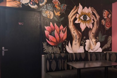 Fresque murale représentant des mains tenant une fleur avec un œil, entourée de papillons et de motifs floraux.