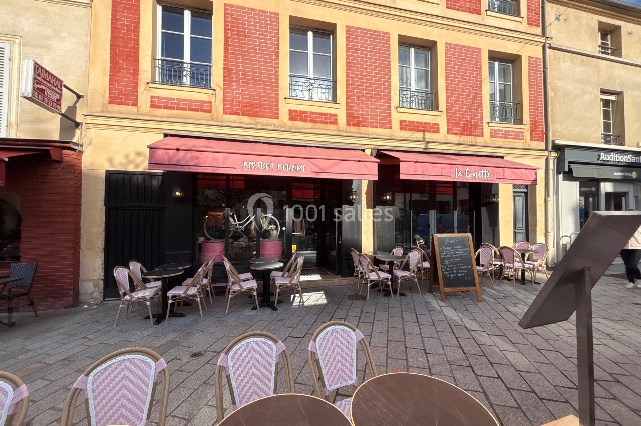 Façade d'un bistrot avec terrasse extérieure, tables et chaises en osier, situé dans une rue pavée.