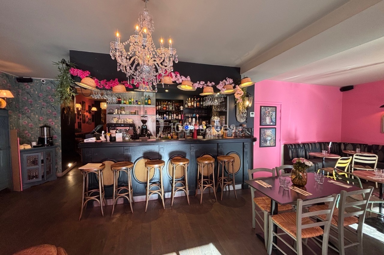 Intérieur d'un bar-restaurant avec comptoir noir, tabourets en bois, lustre et décoration florale colorée.
