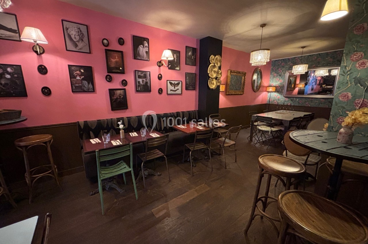 Salle de restaurant chaleureuse avec murs décorés de cadres, tables en bois et éclairage tamisé.