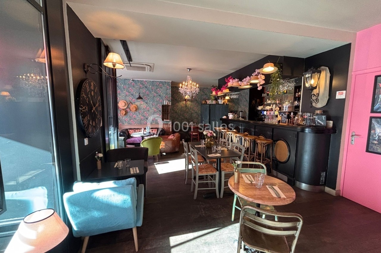 Salle de restaurant lumineuse avec mobilier éclectique, bar en bois, chaises variées et décoration colorée.