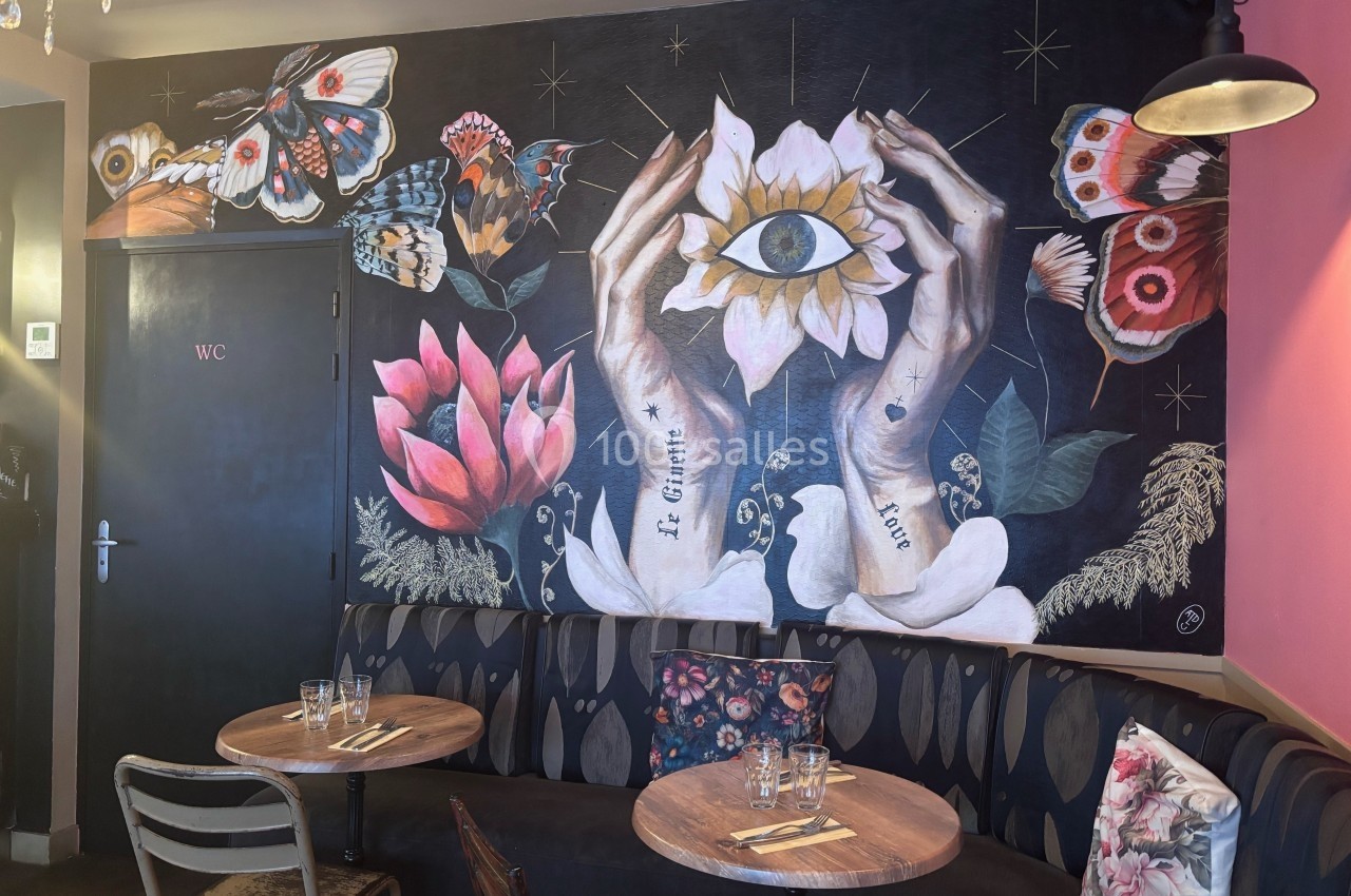 Fresque murale représentant des mains tenant une fleur avec un œil, entourée de papillons et de motifs floraux.