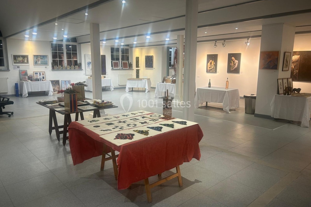 Salle d'exposition lumineuse présentant des œuvres d'art variées sur des murs et des tables.