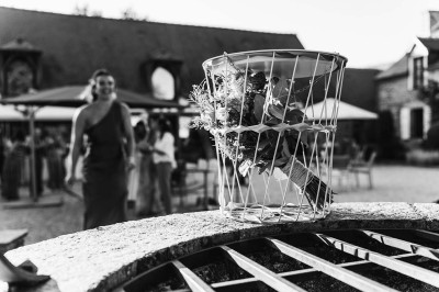 Miniature John Croizé Photographie #6 Un couple en tenue de mariage, l'homme portant la femme dans ses bras devant un mur en pierre ancienne.