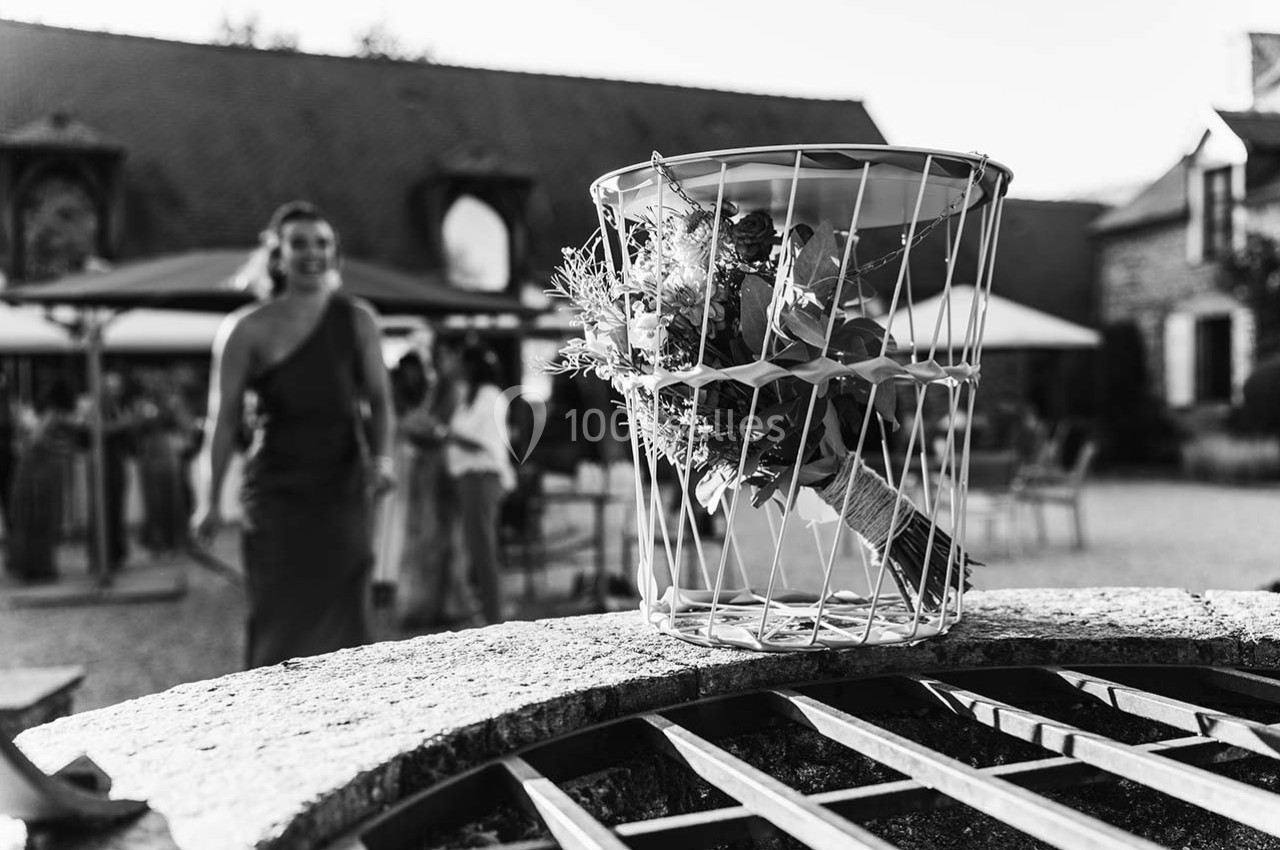 Un bouquet de fleurs posé dans une corbeille métallique sur un puits, avec des invités flous en arrière-plan.