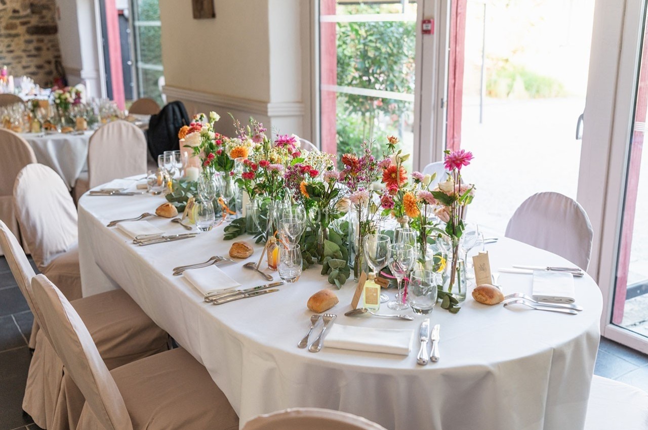 Table de réception décorée avec des fleurs colorées, des verres, des couverts et des serviettes blanches, près de grandes…