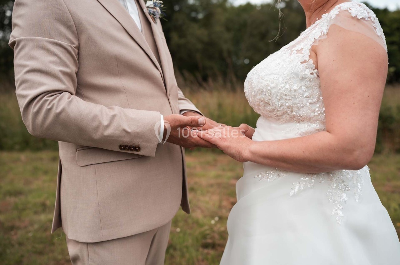 Un couple en tenue de mariage se tenant les mains dans un cadre extérieur verdoyant.