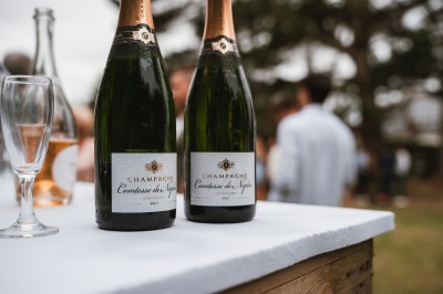 Miniature John Croizé Photographie #7 Un couple en tenue de mariage, l'homme portant la femme dans ses bras devant un mur en pierre ancienne.