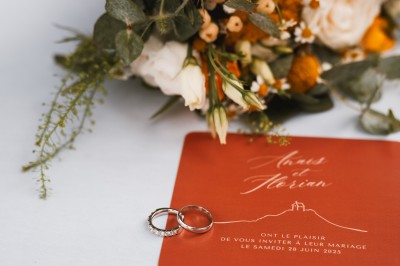Miniature John Croizé Photographie #9 Un couple en tenue de mariage, l'homme portant la femme dans ses bras devant un mur en pierre ancienne.