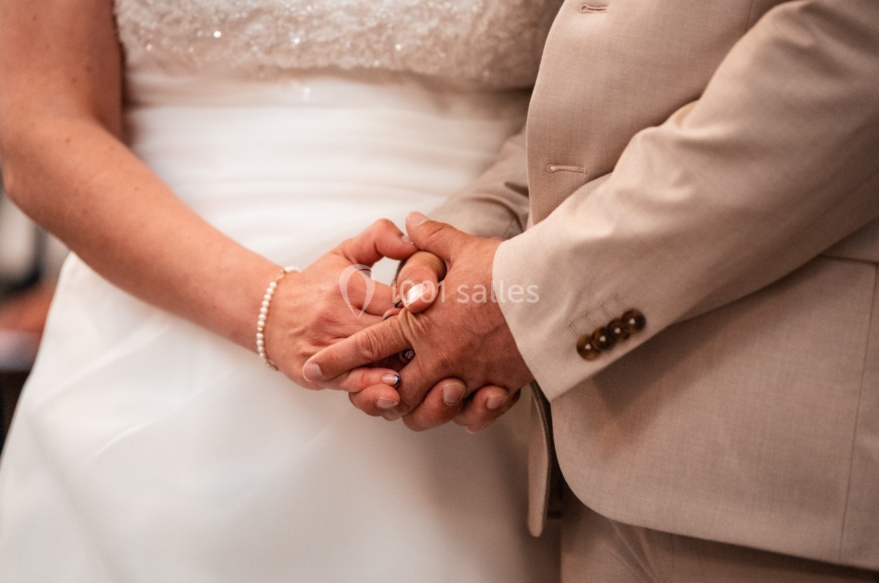 Deux personnes en tenue de mariage se tenant les mains avec tendresse.