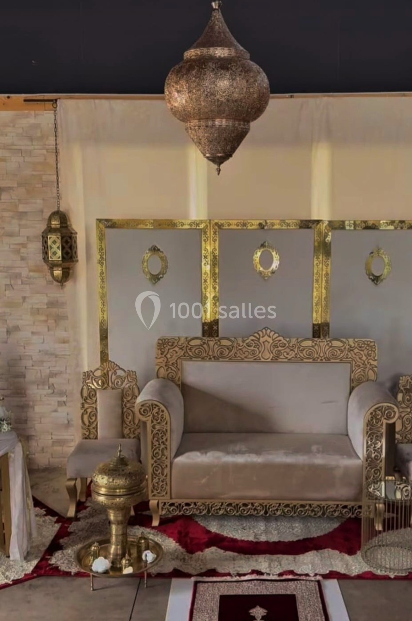 Salon décoré dans un style oriental avec canapé beige, lanternes dorées, tapis rouge et éléments dorés sculptés.