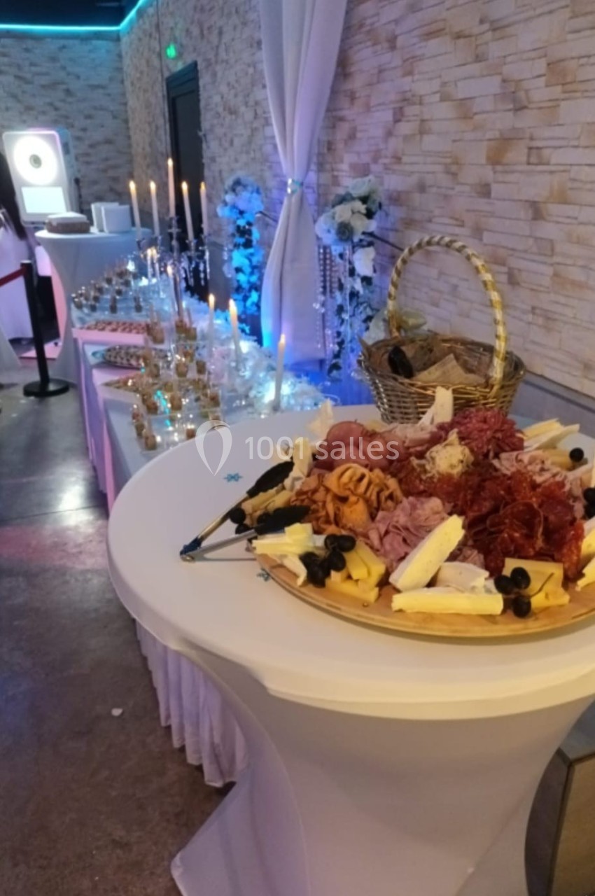 Plateau de charcuterie et fromages sur une table haute, avec buffet décoré et bougies en arrière-plan.