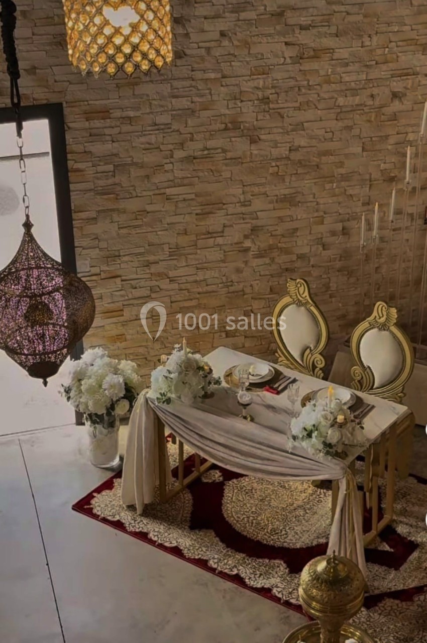 Table décorée avec des fleurs blanches et des chaises dorées, dans une pièce aux murs en pierre et éclairée par des…
