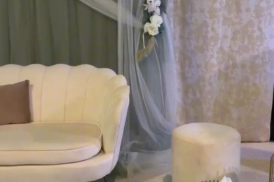 Salle de réception élégante avec tables rondes dressées, chaises transparentes et décorations florales sur chandeliers dorés.