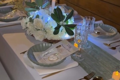 Salle de réception élégante avec tables rondes dressées, chaises transparentes et décorations florales sur chandeliers dorés.