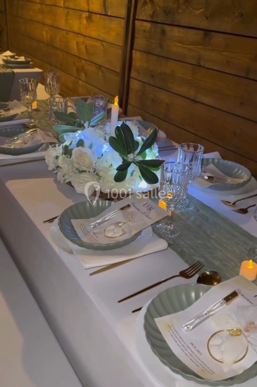 Table décorée avec vaisselle élégante, bougies, menus et centre de table floral blanc sur un chemin de table vert.