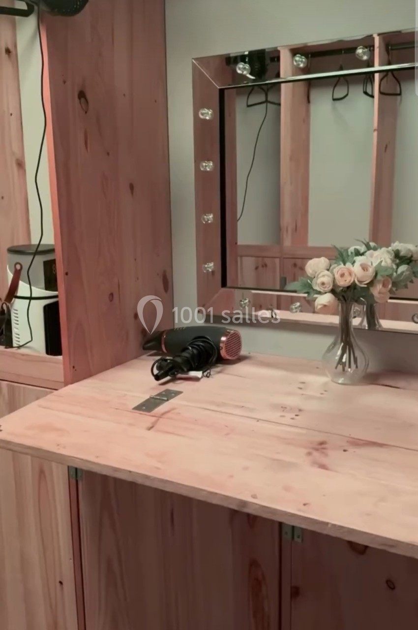 Coiffeuse en bois avec miroir éclairé, bouquet de fleurs, sèche-cheveux et brosse posés sur le plan de travail.