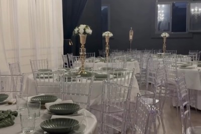 Salle de réception élégante avec tables rondes dressées, chaises transparentes et décorations florales sur chandeliers dorés.