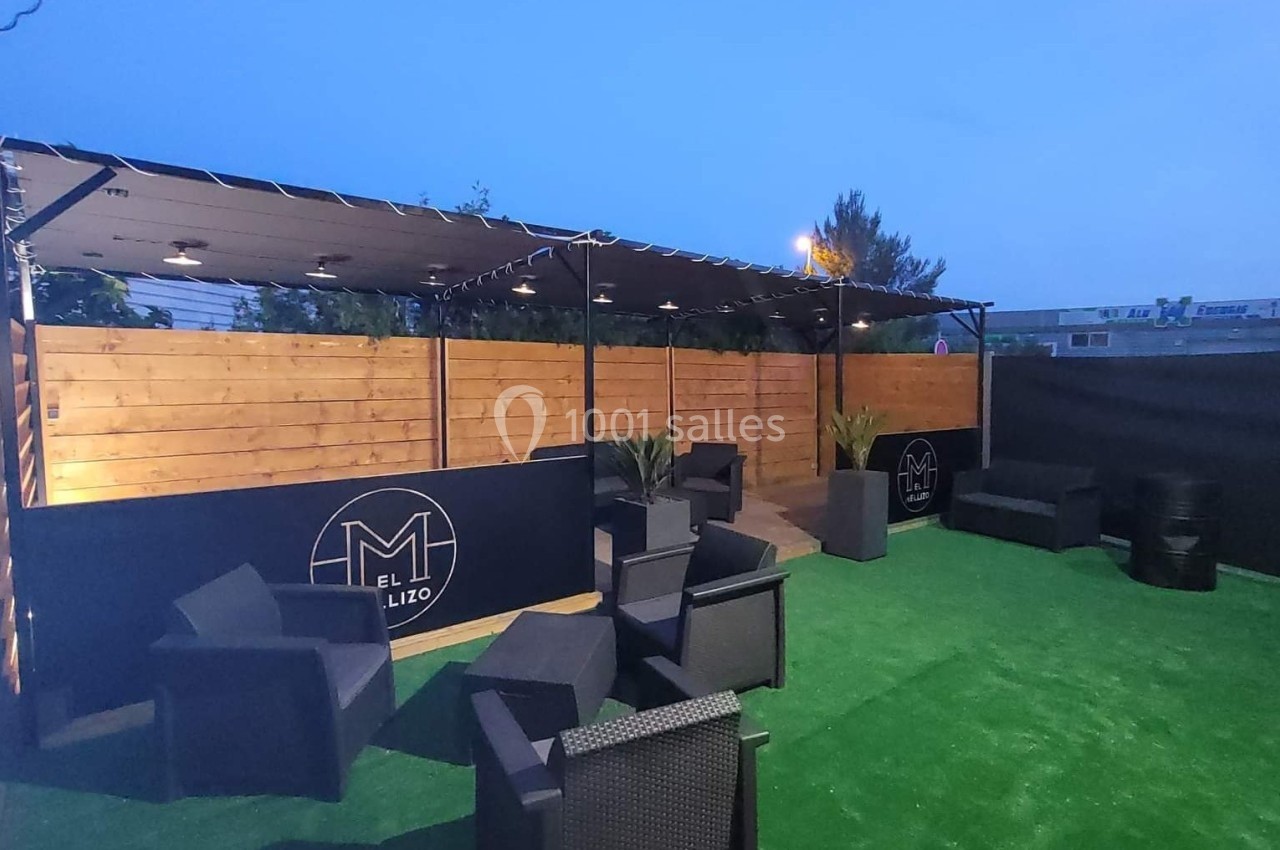 Terrasse extérieure avec mobilier en rotin noir, sol en gazon synthétique et panneaux en bois sous un ciel dégagé.