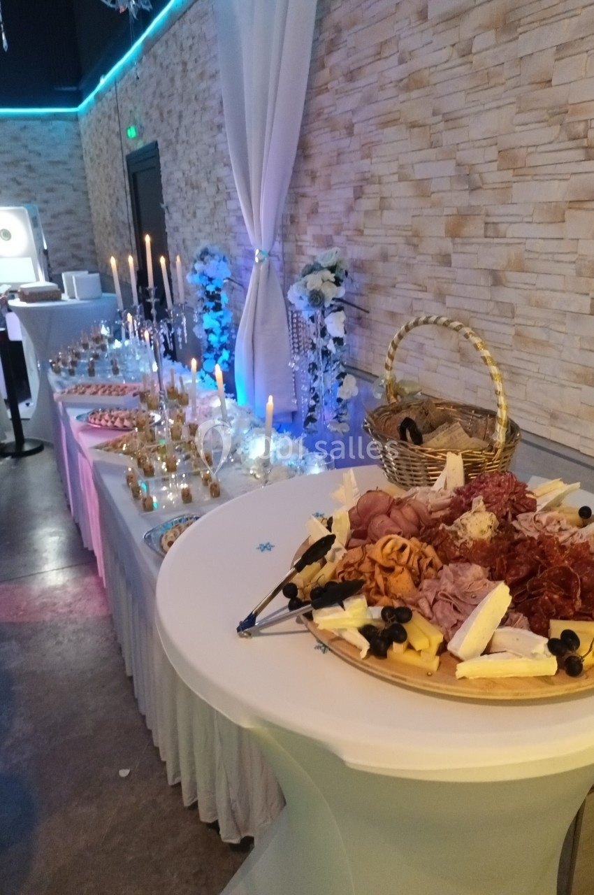 Buffet avec charcuterie, fromages, olives et bougies, disposé sur une table décorée dans une salle éclairée.