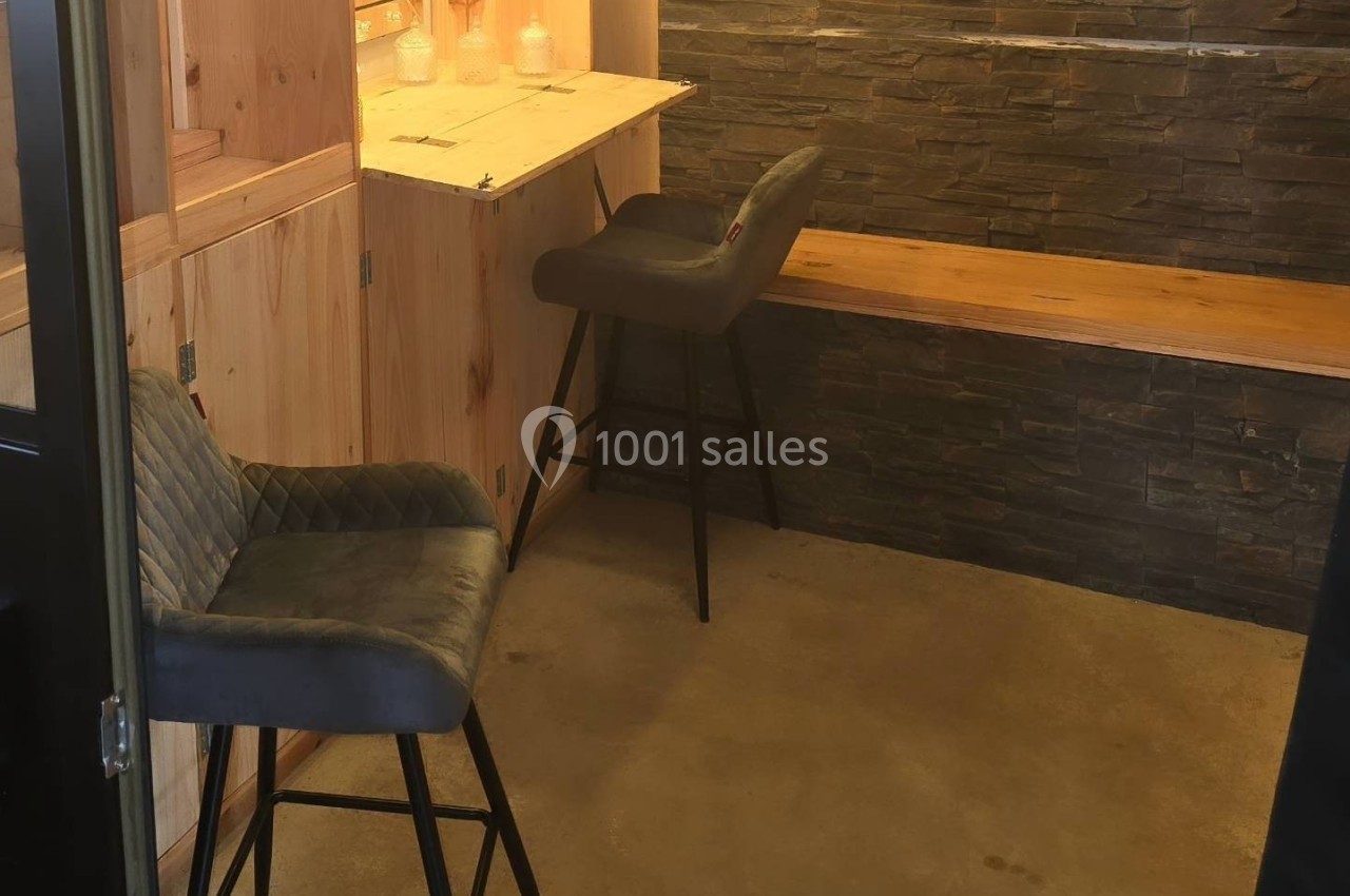 Deux chaises hautes grises devant un comptoir en bois clair, avec un mur en pierre et un sol en béton.