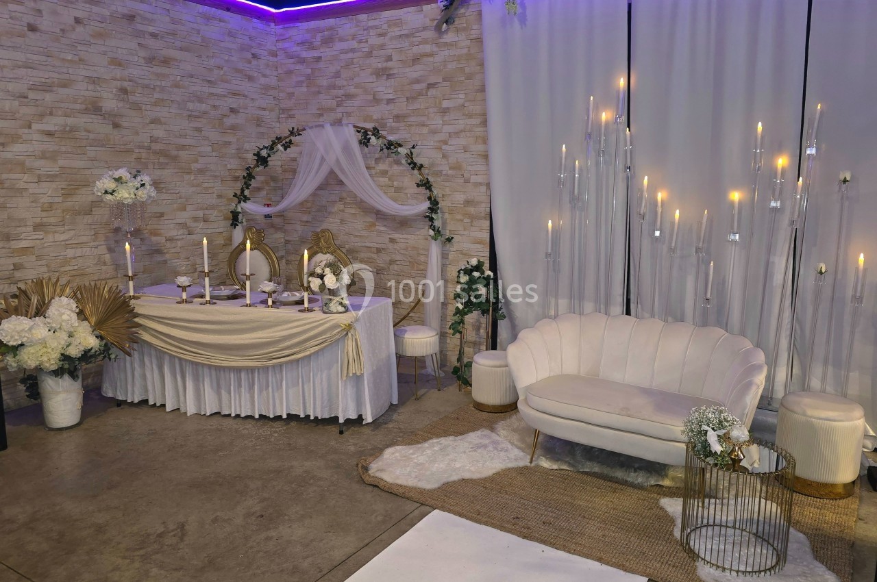 Décoration de salle avec table ornée de bougies et fleurs, canapé blanc et rideaux éclairés par des lumières tamisées.