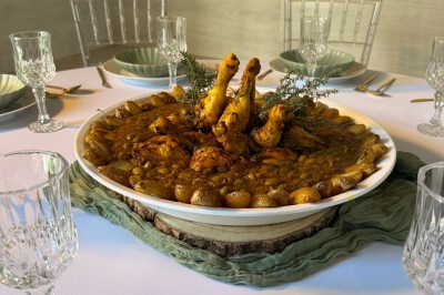 Plat de poulet mijoté avec légumes et épices, présenté dans un grand plat rond sur une table dressée.