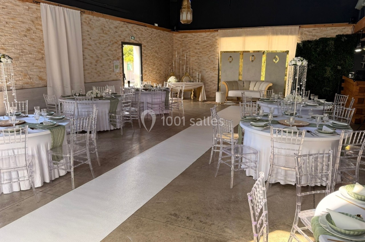 Salle de réception décorée pour un mariage avec tables rondes, chaises transparentes et allée centrale blanche.
