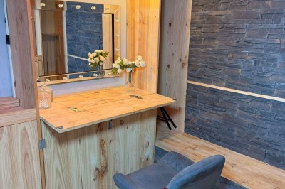 Coiffeuse en bois avec miroir éclairé, chaise grise et mur en pierre décorative en arrière-plan.