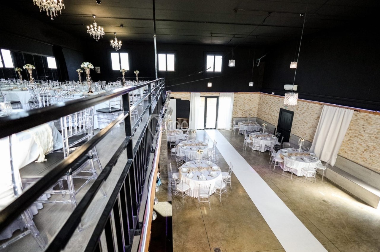 Salle de réception moderne avec tables rondes dressées, chaises transparentes et éclairage élégant sous un plafond noir.