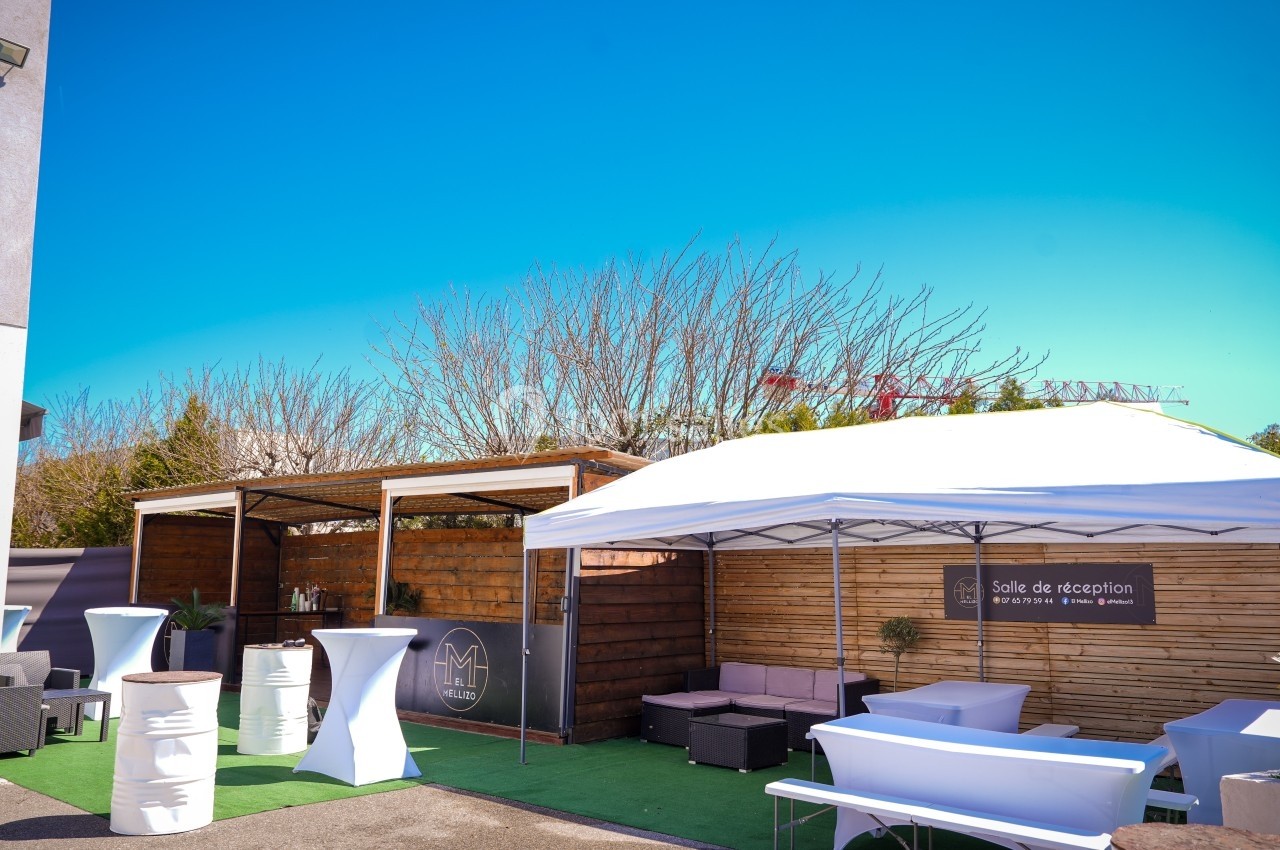 Espace extérieur aménagé avec mobilier de réception, tonnelle blanche et décor en bois sous un ciel dégagé.