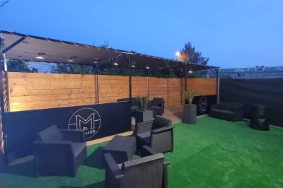 Coiffeuse en bois avec miroir éclairé, chaise grise et mur en pierre décorative en arrière-plan.