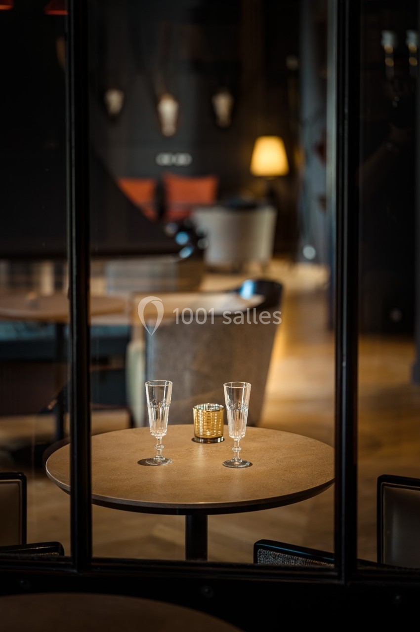 Deux verres à pied et une bougie dorée sur une table ronde dans un intérieur chaleureux et tamisé.