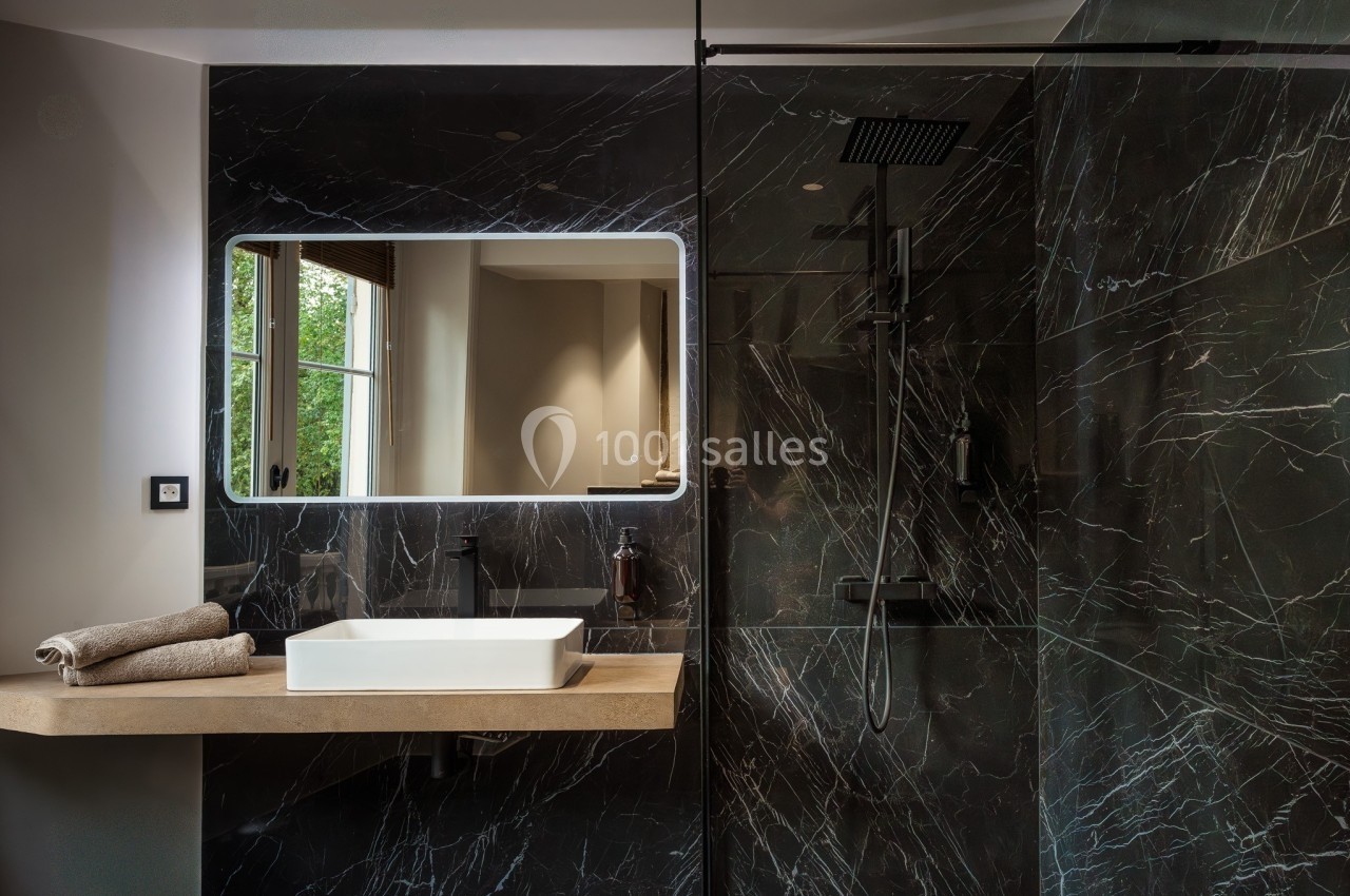Salle de bain moderne avec lavabo sur plan en bois, miroir éclairé et douche à paroi en marbre noir.